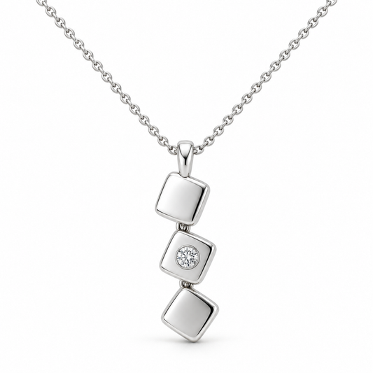 [metal:white-gold] Iserelle Offset Tile Pendant — front — Three small solid polished rounded-square metal tiles in a stepped diagonal cascade, hinged by tiny concealed links, each tile rotated slightly differently. Middle tile alone has one small flush-set round diamond. Fine cable chain through top tile bail. [catalog-v4]; any chain shown is an optional styling accessory