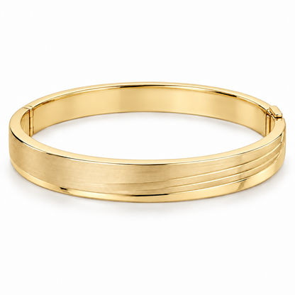 [metal:yellow-gold] Lorisse Offset-Step Bangle — front — Closed oval hinged bangle, broad flat satin top with three shallow parallel stepped terraces offset toward one edge, polished smooth borders, discreet side hinge and opposite box clasp. Steps are metal surface levels, not multiple separate bangle bands. No stones. [catalog-v4]